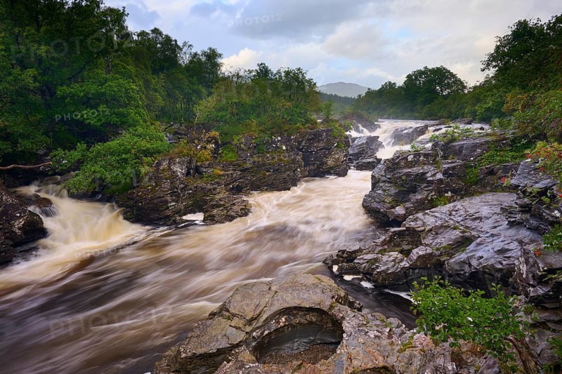 A wild river flows through a rocky landscape surrounded by lush greenery and cloudy skies, River Orchy, Eas Urchaidh, Bridge of Orchy, Scotland, United Kingdom, Great Britain