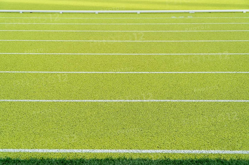 Close-up of vibrant green synthetic running track with white lanes in an outdoor athletics stadium. No persons are visible in the image