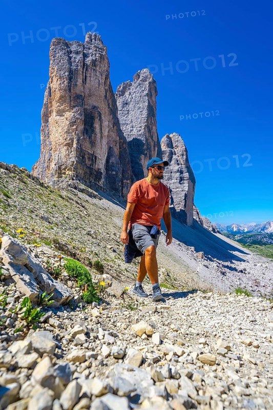 Tourist walking on the scenic trail leading to the tre cime di lavaredo, enjoying the breathtaking mountain landscape in the italian dolomites
