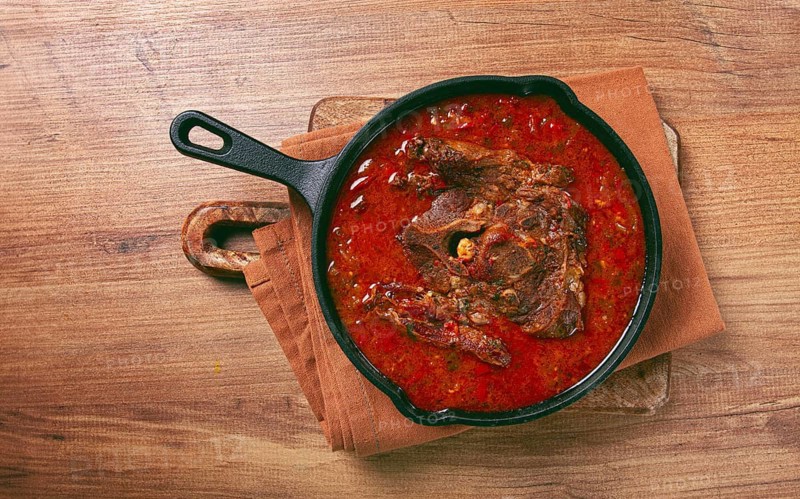 Fried steak, veal neck on the bone, stewed with vegetables, in tomato sauce, cooking meat, in a cast-iron frying pan, top view, no people