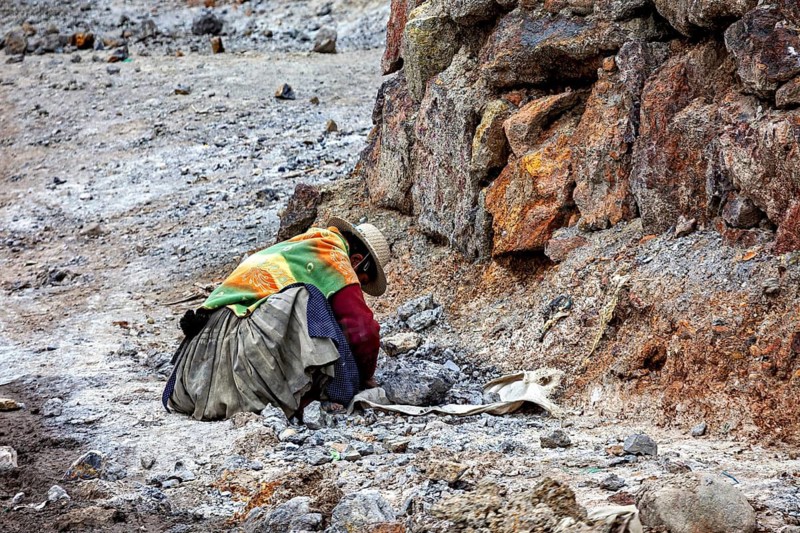 A person wearing colorful clothes works in a rocky environment, the Potosi silver mines on Cerro Rico in Bolivia
