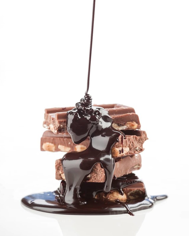 A tantalizing stack of chocolate bars topped with rich, dark chocolate syrup, oozing down and pooling at the base, set against a clean, white background