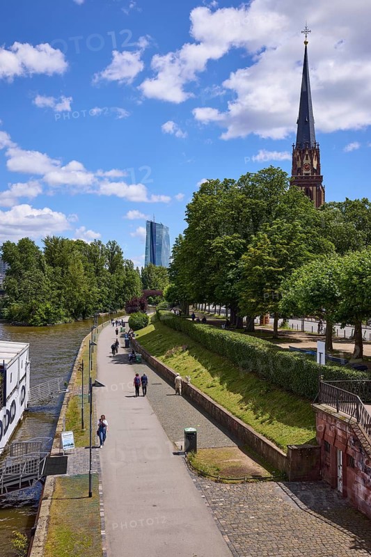 Main river with riverside promenade and Evangelische Dreikönigskirche under blue sky with cumulus clouds in Frankfurt am Main, Hesse, Germany