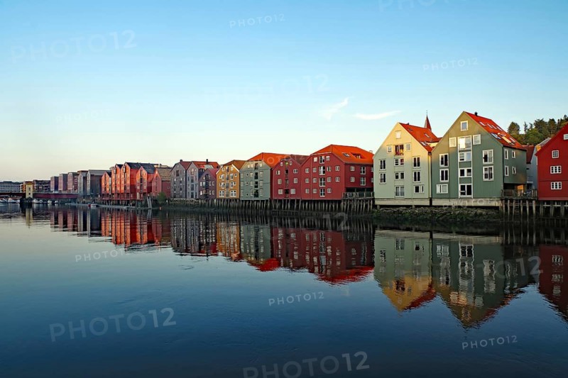 Row of colorful houses along a quiet river with reflections in the water, Nidelva, Trondheim, Tröndelag, Norway
