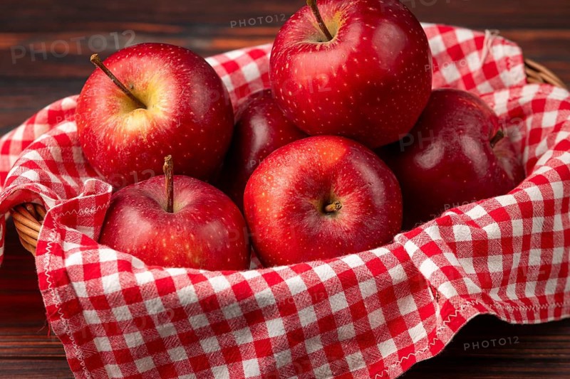 Fresh red apples in a basket with red checkered cloth on wooden background