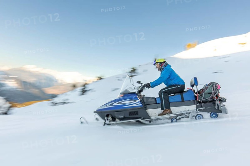 A snowmobile rider in a blue jacket speeds through a snowy landscape, showcasing the thrill of winter sports in a pristine environment. Ideal for adventurous enthusiasts