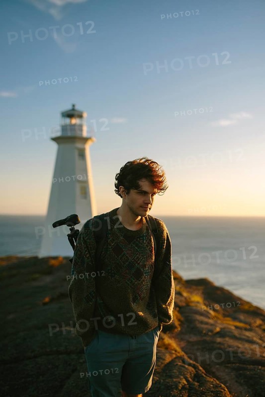 A young man stands by the Cape Spear Lighthouse in Newfoundland & Labrador, Canada, enjoying a serene ocean view during sunset
