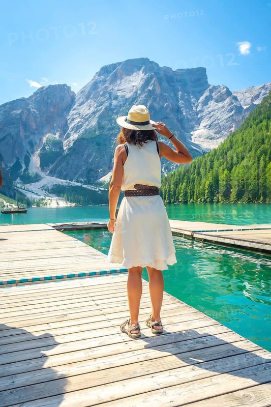 Tourist standing on a wooden pier, enjoying the breathtaking view of lake braies and the surrounding dolomites mountains in summer