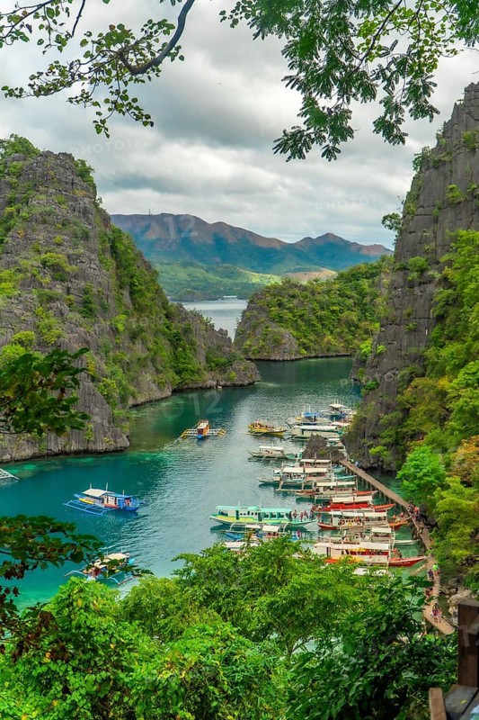 Tourists exploring kayangan lake in coron island, philippines, surrounded by stunning rock formations and lush vegetation, enjoying a boat trip on a cloudy day