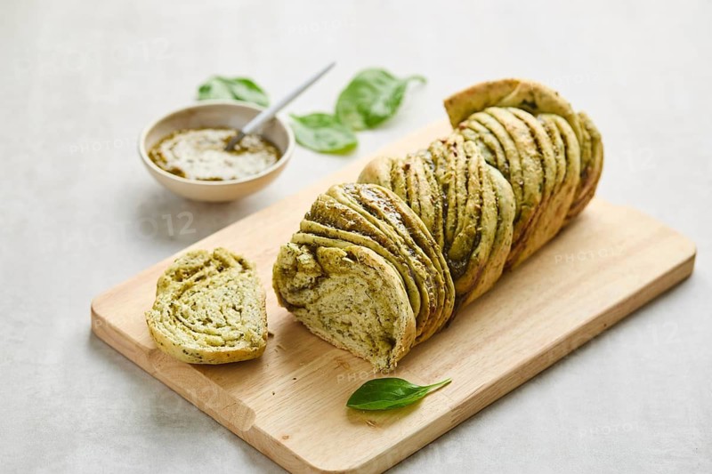 Baked homemade savoury babka plaited bread loaf flavoured with pesto on wooden bread board