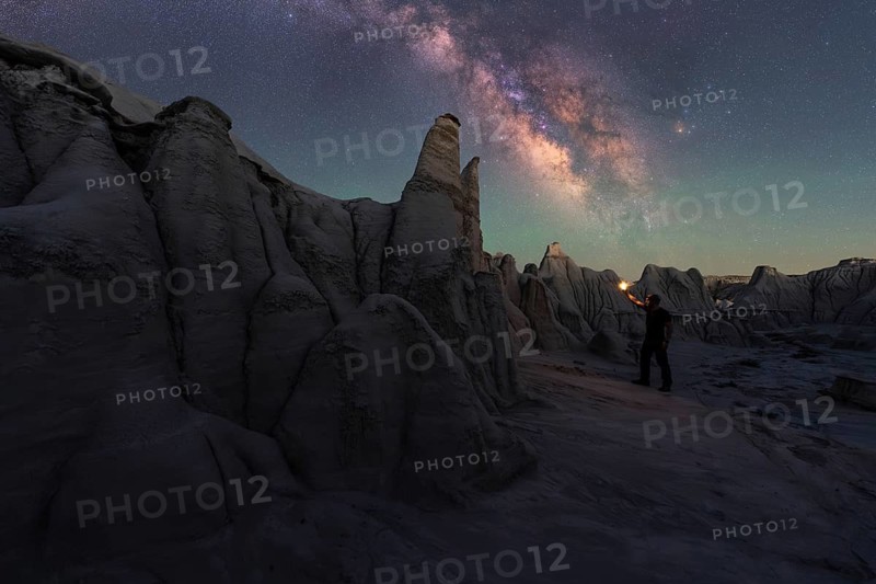 A breathtaking view of Goblin Valley's sandstone structures under a captivating night sky. A lone figure illuminates the scene, enhancing the cosmic beauty