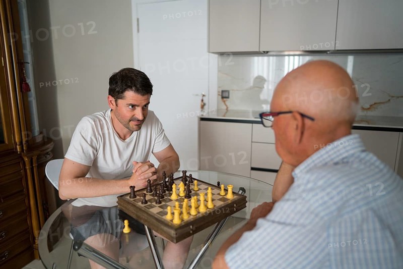 An intimate moment of an elderly father and adult son sharing quality time, engaging in a thoughtful chess game at home, showcasing intergenerational bonding and connection