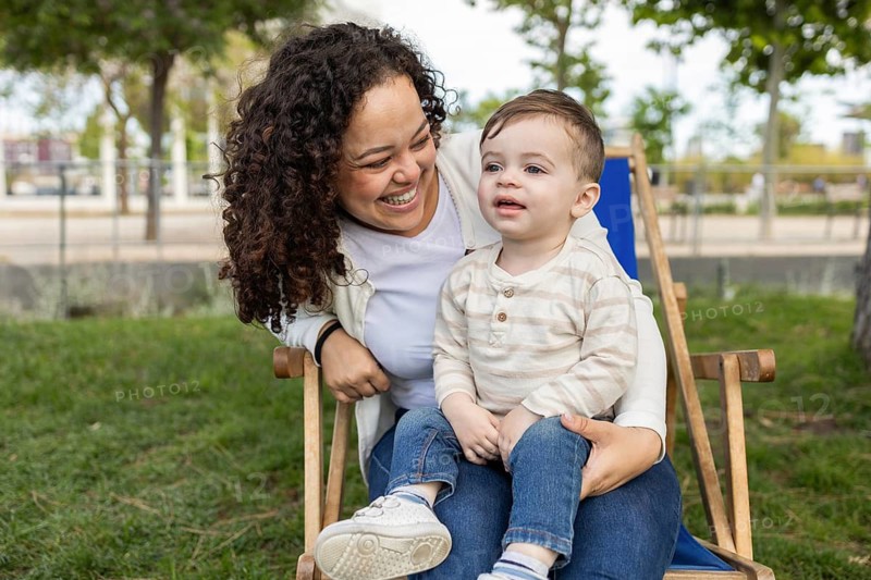 A joyful mother and her baby enjoy a sunny day in the park, sharing laughter and creating cherished memories seated on a wooden chair surrounded by lush greenery