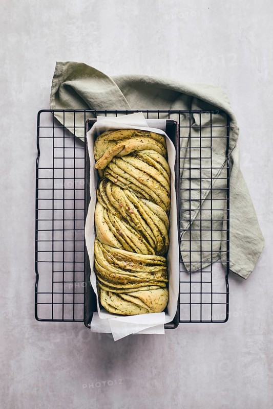 Baked homemade savoury babka plaited bread loaf flavoured with cheese and pesto, in the making tin
