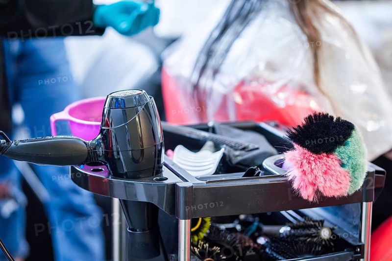 Professional hair stylist tools arranged on a salon trolley in beauty salon. Hair dryer, combs and brushes in hairstylist workspace with client in background, hairdressing equipment and salon service concept