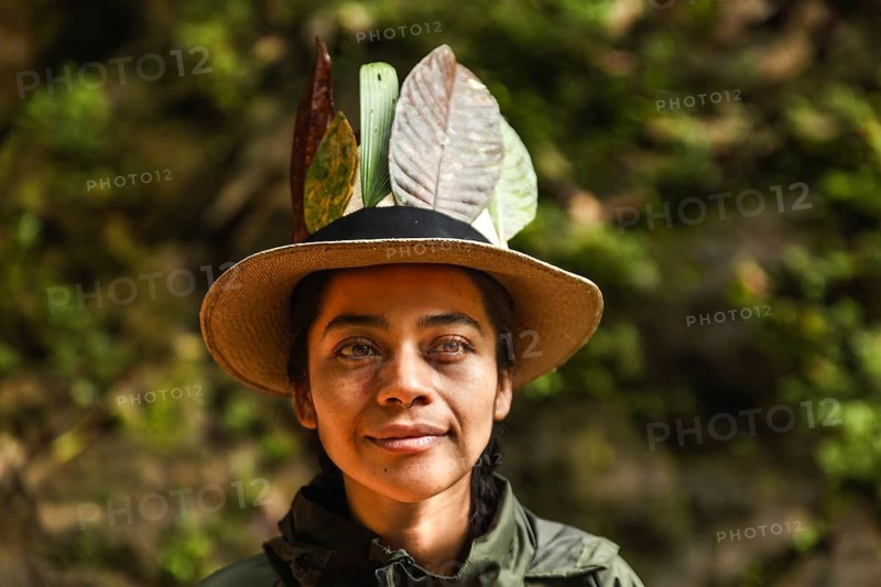 Close-up portrait of a young Ecuadorian woman adorned with leaves in her hat, set against the green backdrop of the Choco Andino rainforest in Ecuador. She represents local culture and sustainable tourism amidst a lush, natural environment