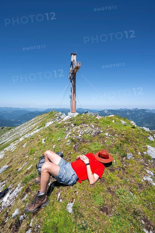 Mountaineer taking a nap at the summit, resting after a mountain tour, Hochunnütz summit with summit cross, Unnütz crossing, Brandenberg Alps, Tyrol, Austria