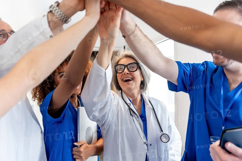 Happy mature female doctor high fiving with a diverse healthcare team, symbolizing unity, success, and partnership in medicine, showcasing their strong teamwork and commitment to patient care