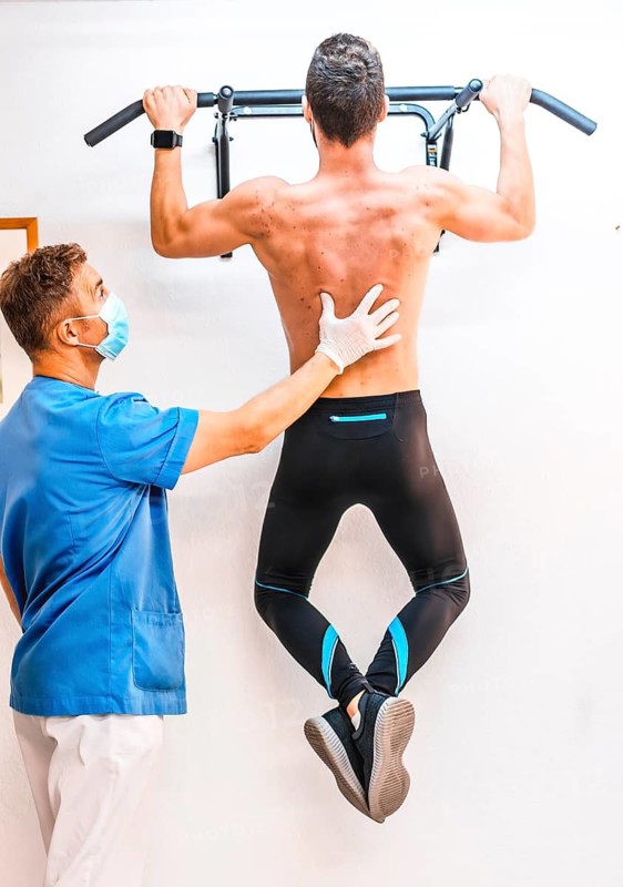 Physiotherapist helping a shirtless patient with a dominated one. Physiotherapy with protective measures for the Coronavirus pandemic, COVID-19. Osteopathy, therapeutic chiromassage