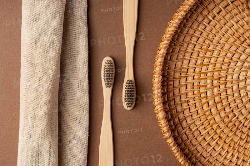 Top view of bamboo toothbrushes on a brown background, accompanied by a woven basket and a linen cloth, highlighting eco-friendly and sustainable bathroom essentials