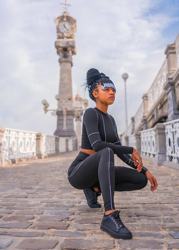 Beautiful Dominican Ethnic Girl with with braids with full body suit. Fashion Posé Druzed next to a beautiful beach clock