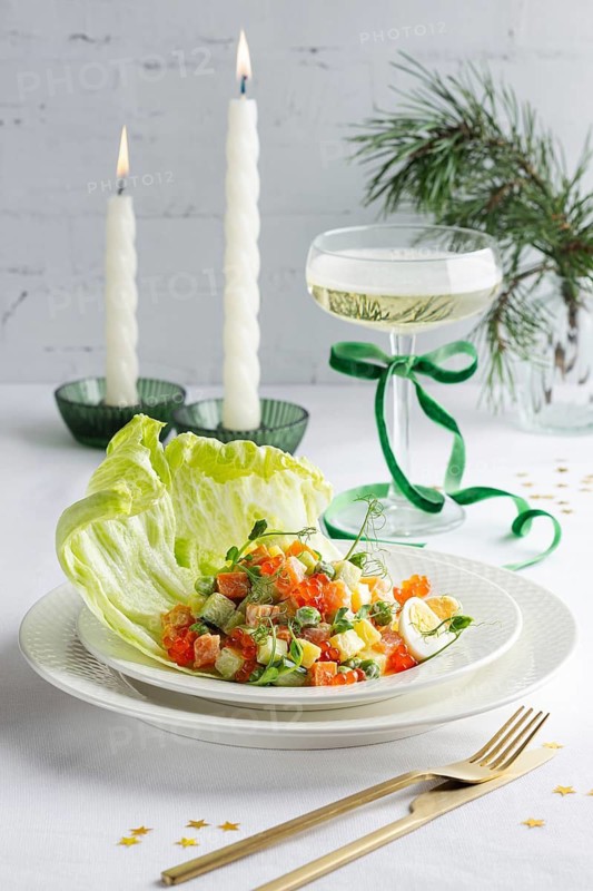 A beautifully arranged plate of salmon Olivier salad, garnished with fresh greens and egg, served alongside lit candles and a festive glass of wine