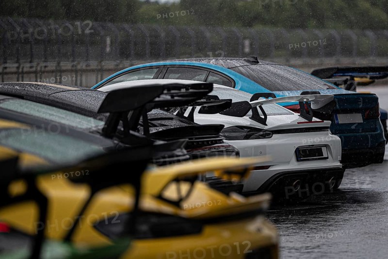 A stunning lineup of various sports cars, drenched by rain, parked on a race track, showcasing an array of vibrant colors and advanced aerodynamic designs in a moody, wet environment