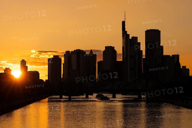 The sun sets behind the skyscrapers of Frankfurt's banking skyline as a barge sails along the Main, Frankfurt am Main, Hesse, Germany