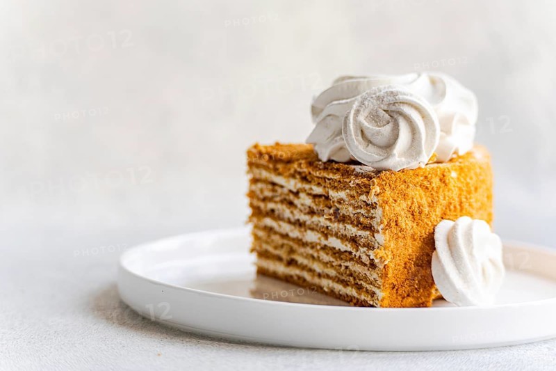 A delectable homemade honey cake topped with a generous dollop of sour cream sauce and elegantly decorated with a rich vanilla zephyr on a pristine white plate