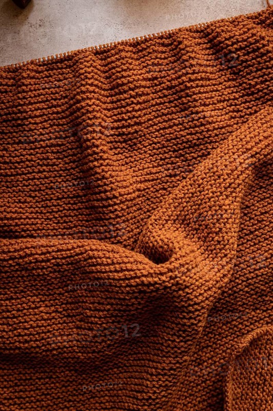A close-up view of a cozy, brown knitted fabric, showcasing its intricate texture. Perfect for themes of warmth, comfort, craftsmanship, or autumn designs