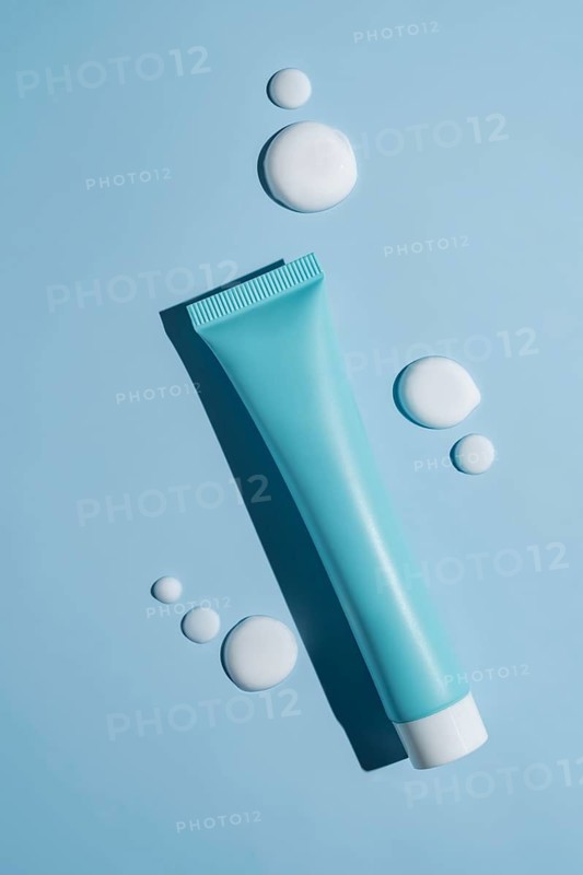 A sleek cosmetics package sits elegantly on a blue background, accented by smooth, artistic smears of white cream. The scene embodies modern beauty concepts