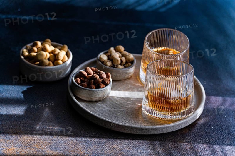 Spiced cognac cocktail featuring cinnamon and star anise, accompanied by almonds, peanuts, and hazelnuts in rustic bowls on a textured tray