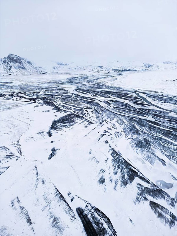 Aerial view of a vast Icelandic winter landscape blanketed in snow, showcasing intricate river patterns and rugged terrain, creating a serene, remote wilderness scene, VÃ­k Ã­ MÃ½rdal, SuÃ°urland, Islandia
