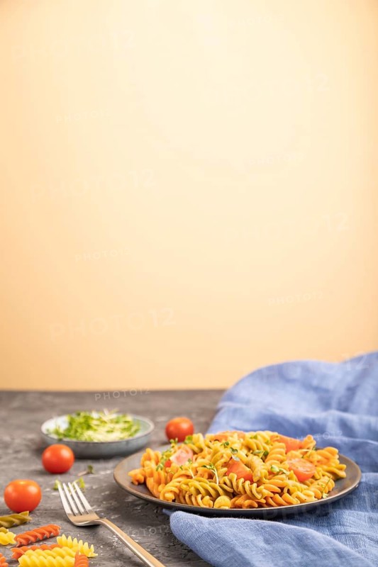 Tortiglioni semolina pasta with tomato and microgreen sprouts on a black and orange background and blue textile. Side view, copy space, selective focus