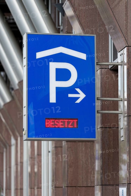 Blue car park sign with white P symbol and red display with the words 'Occupied' in front of modern architecture, Baden-Württemberg, Germany