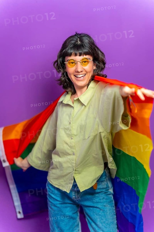 Studio portrait with purple background of a non binary latin woman dancing wrapped with lgbt rainbow flag