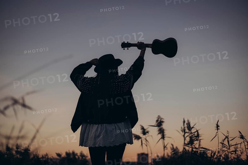 A silhouette of a woman raising her ukulele against a stunning sunset backdrop, capturing a moment of freedom and expression in nature. The scene evokes a sense of peace and adventure