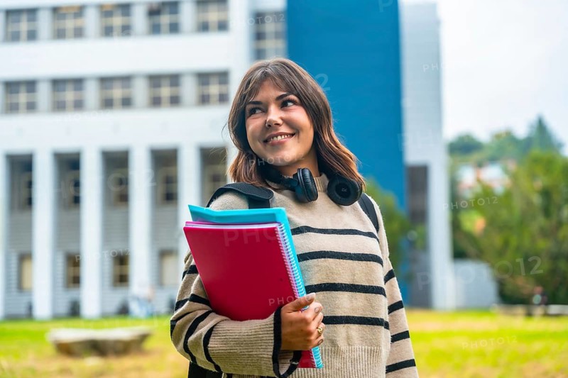 Happy young student woman is walking on a university campus, holding notebooks and wearing headphones, symbolizing education, learning, and a bright future in higher academe