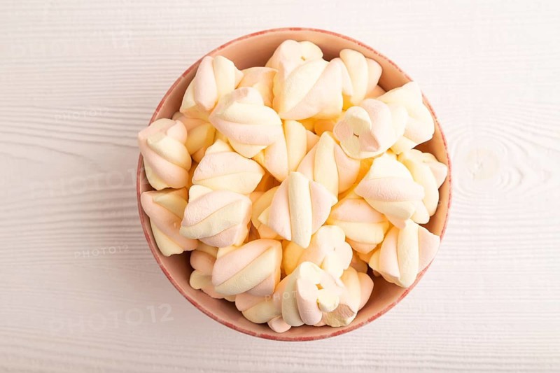 Orange and pink marshmallow in ceramic bowl on white wooden background, top view, flat lay, copy space, minimalism