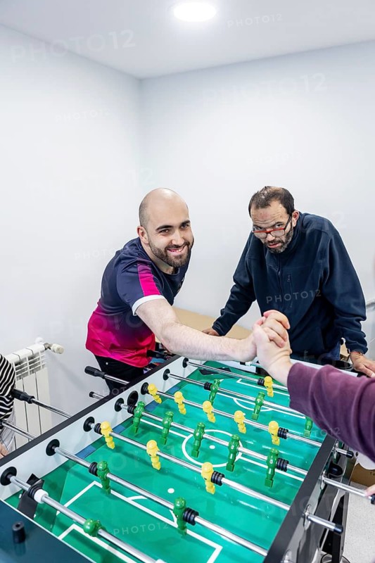 Residents enjoy a lively foosball game in a mental health facility, fostering camaraderie, relaxation, and social engagement in a supportive environment
