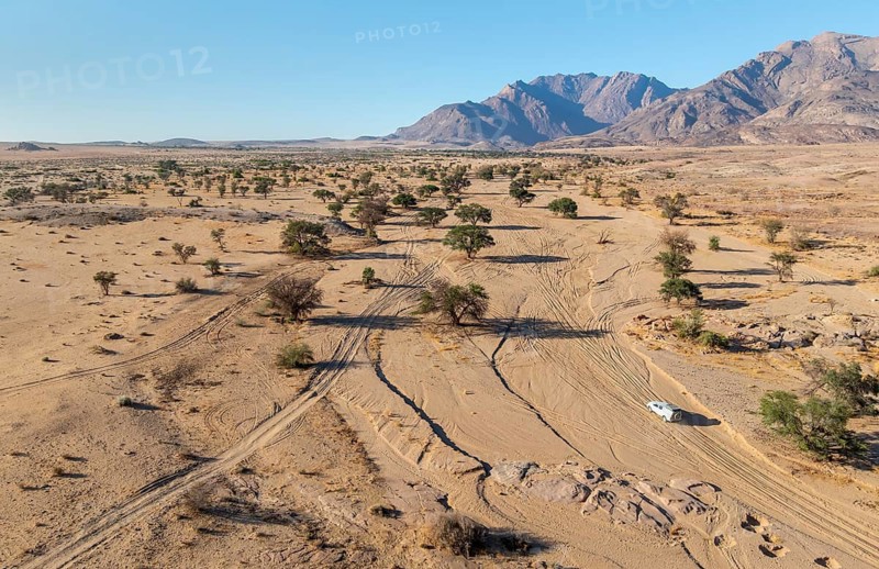 Aerial view of off-road car driving in dry riverbed and desert landscape on the Ugab River, behind Brandberg, Erongo, Damaraland, Namibia
