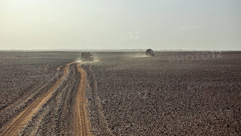 Two vehicles travelling on a dusty sandy road through a vast, open desert landscape, Off-road vehicle through the Sahara desert in Algeria