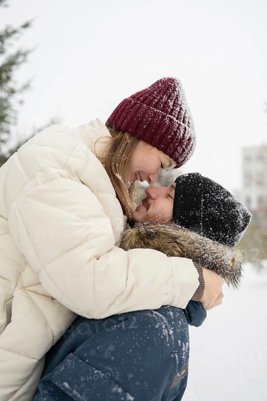 A loving couple shares a joyful embrace in a snowy outdoor setting Their warm winter clothing, including hats and coats, contrasts beautifully with the white snowflakes