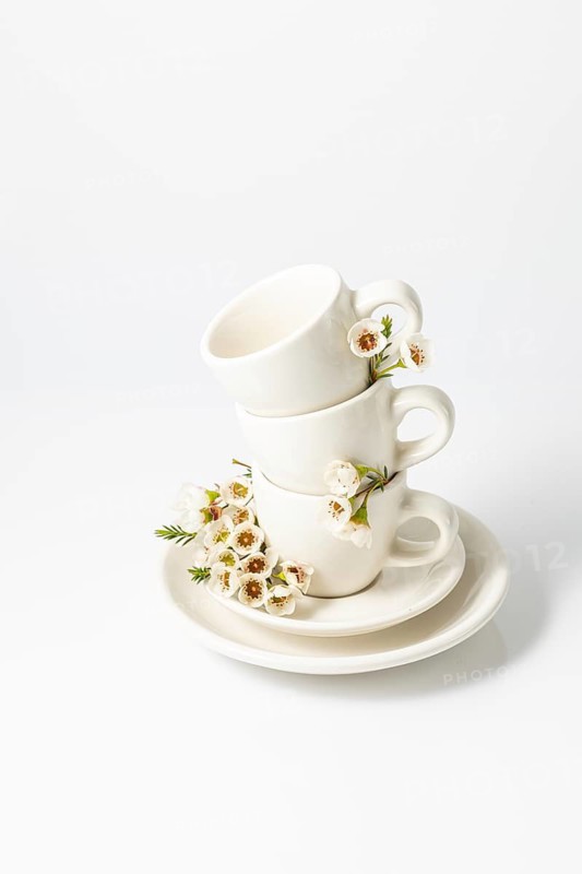 Stack of white ceramic cups and a saucer, elegantly garnished with fresh spring flowers on a white background, reflecting a serene and aesthetic vibe