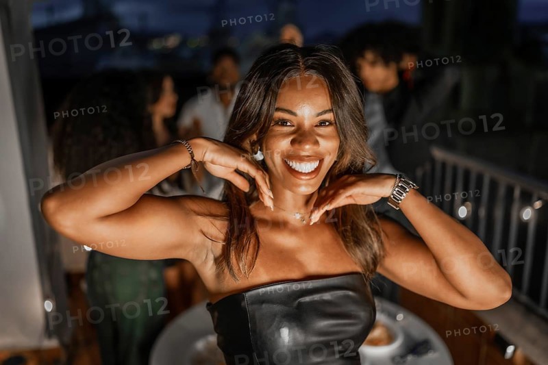 Happy beauty latin woman smiling at camera while partying at night with multi-ethnic friends in a rooftop