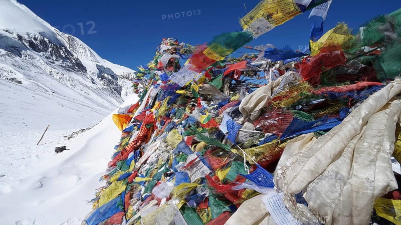 Colourful prayer flags fly near snow and mountain scenery in the Himalayas, Thorong La, Manang, trekking at Annapurna Circuit, Nepal