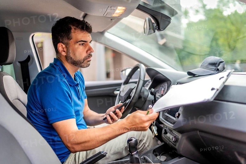 Delivery man using mobile phone and doing paperwork before deliver packages sitting inside a car
