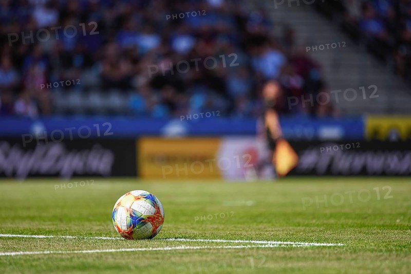 Ball on the soccer pitch with sideline referee and tribune in the background