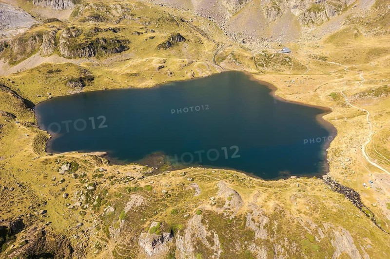 Aerial view of a tranquil mountain lake at Ayous refuge in the French Pyrenees The emerald waters are surrounded by rocky terrain and lush greenery, under a clear sky