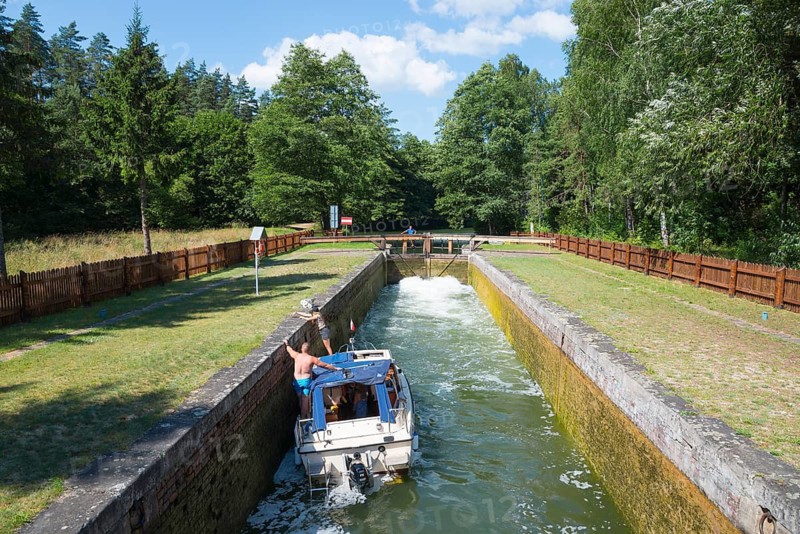 A boat navigates through the lock with green surroundings and blue sky in the background, Sluza Paniewo, lock between the lakes Paniewo and Krzywe, Plaska, Powiat Augustowski, Podlaskie Voivodeship, Poland